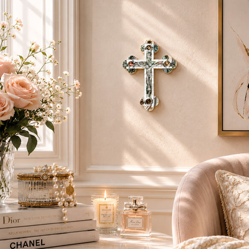 Decorative cross on a wall with flowers, books, and candles in a room.