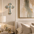 Decorative cross on a wall above a bed with a lamp and artwork.