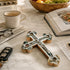Decorative cross on a marble surface with a cup, glasses, and book in the background.