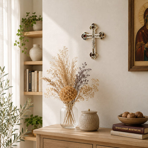 Decorative setting with a vase of dried flowers, a cross on the wall, and books on a wooden surface.