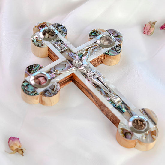 Full size handcrafted olive wood budded cross adorned with a detailed silver crucifix and colourful mother of pearl, resting on a clean white surface with scattered rose petals for a serene touch.