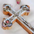 Zoomed image of a handcrafted olive wood budded cross with a silver crucifix and colourful mother of pearl, resting on a clean white surface.