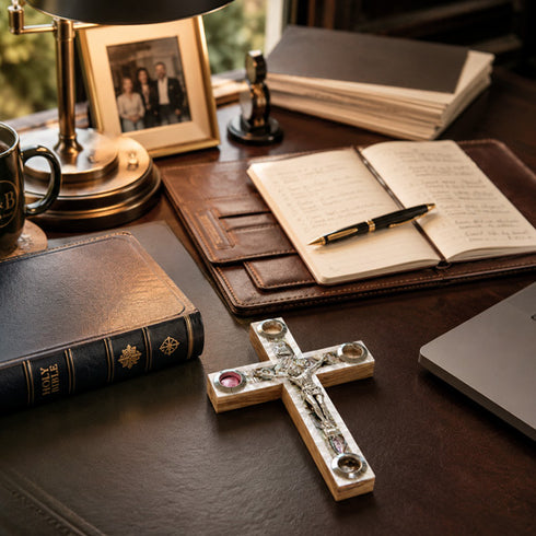 Desk with a cross, notebook, pen, and other items on a wooden surface.