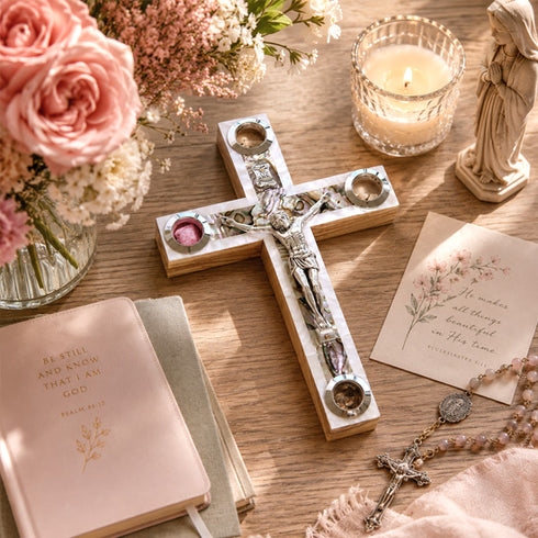 Decorative cross with religious text, candles, flowers, and a statue on a wooden surface.