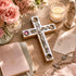 Decorative cross with religious text, candles, flowers, and a statue on a wooden surface.