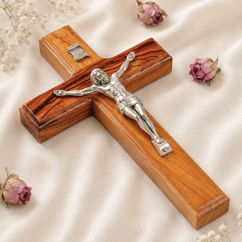 A handcrafted olive wood Latin crucifix with Jesus Christ on the cross, set against a white background with flowers.