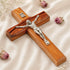 A handcrafted olive wood Latin crucifix with Jesus Christ on the cross, set against a white background with flowers.