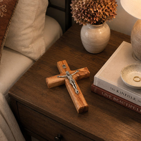 Wooden cross with Jesus figure on a wooden surface with books and decor items.