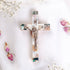 Small olive wood cross with crucifix, Nacre inlay and INRI plaque, laid on white surface with rose petals around it.