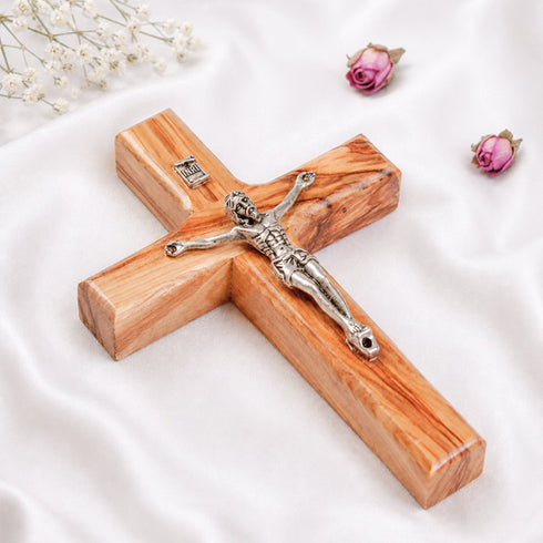 A handmade Latin crucifix made from Bethlehem olive wood, featuring silver figure of Jesus Christ, laid on white background with flowers.