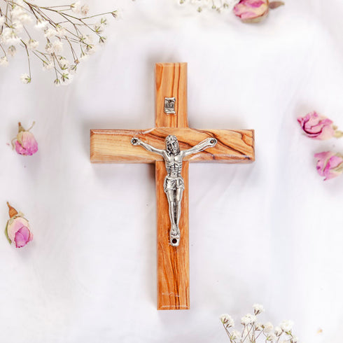 Small olive wood latin cross with metal crucifix and INRI plaque, laid on white surface with rose petals around it.