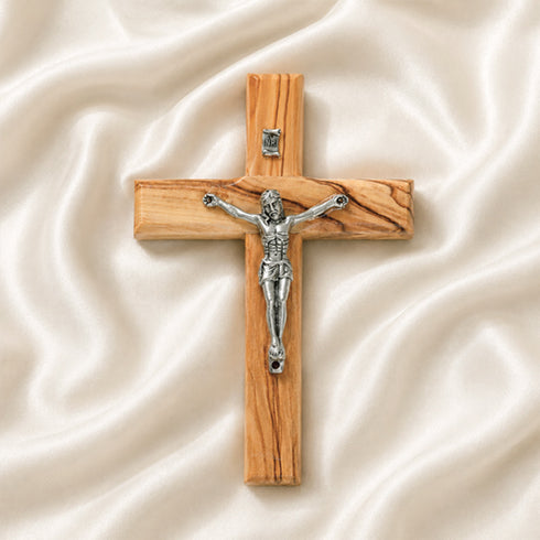 Small olive wood latin cross with metal crucifix and INRI plaque, laid on white surface with rose petals around it.