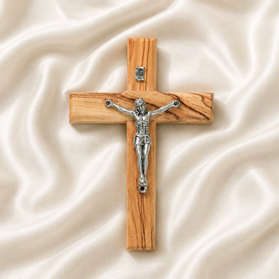 Small olive wood latin cross with metal crucifix and INRI plaque, laid on white surface with rose petals around it.