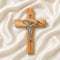 Small olive wood latin cross with metal crucifix and INRI plaque, laid on white surface with rose petals around it.