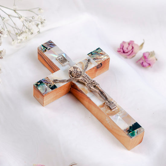 Olive Wood Latin Crucifix with Mother of Pearl shell adornments, placed on a white fabric with flowers.