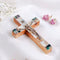 Olive Wood Latin Crucifix with Mother of Pearl shell adornments, placed on a white fabric with flowers.