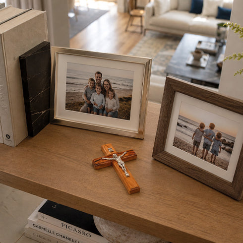 Framed family photos on a wooden surface with a cross and books in the background.