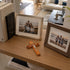 Framed family photos on a wooden surface with a cross and books in the background.