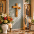 Decorative setting with religious statues, cross, flowers, and candles on a marble surface.