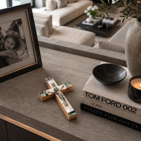 Decorative cross, books, and candle on a table with a blurred living room background