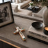 Decorative cross, books, and candle on a table with a blurred living room background
