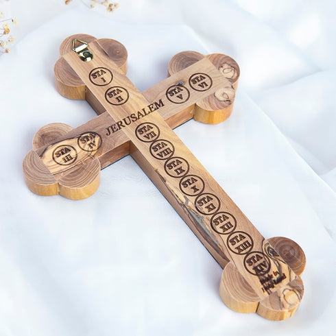 A handcrafted olive wood Eastern cross with Jerusalem and the Station of Cross engraved at the back. Set on a white fluffy background.