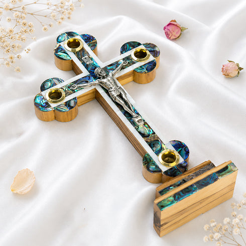 A handcrafted standing wooden cross with mother-of-pearl inlays, four holy elements on a white background with dried flowers.