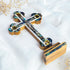 A handcrafted standing wooden cross with mother-of-pearl inlays, featuring the four holy elements and silver coloured crucifix. It is set against a white fluffy background with dried flowers.