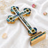 A handcrafted standing wooden cross with mother-of-pearl inlays, four holy elements on a white background with dried flowers.