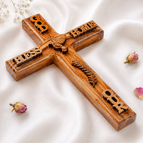 A wooden cross with 'GOD BLESS OUR HOME' inscribed on its arms, featuring intricate carvings and a dove design.