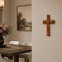 Wooden cross on a wall above a dining table with flowers and a painting in the background.