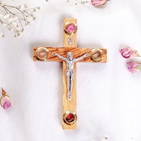 Medium Latin cross hand-crafted from Bethlehem olive wood with silver crucifix and Holy Soil, on white backdrop with petals.
