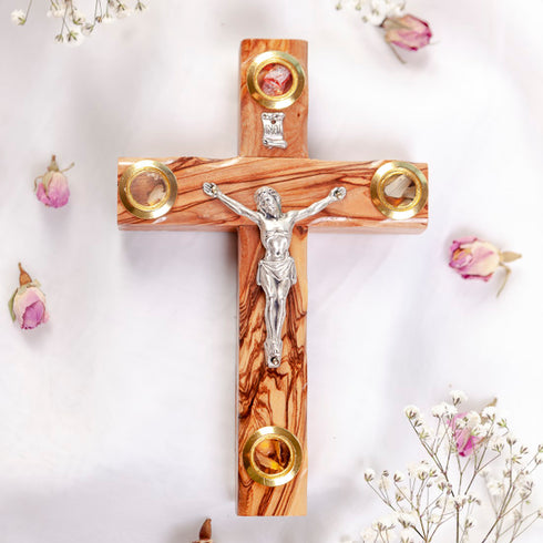 Frontal presentation of a small olive wood Latin crucifix with Four Elements on a white surface with rose petals.