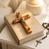 Wooden cross with red stones on an open Bible, surrounded by a rosary and a candle.