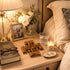 Nighstand with a Bible, glasses, wooden cross, photo frame, and candle.