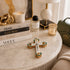 Decorative cross on a marble table with books, candles, and a lamp in the background.