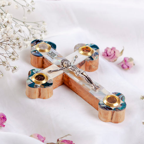 A handcrafted olive wood crucifix with mother of pearl decoration, placed on a white fabric with flower petals.