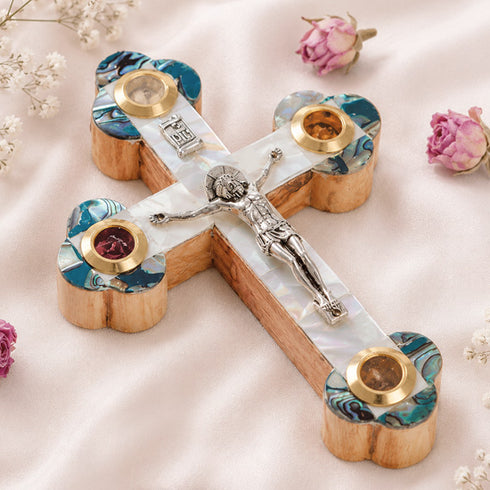 A handcrafted olive wood crucifix with mother of pearl decoration, placed on a white fabric with flower petals.
