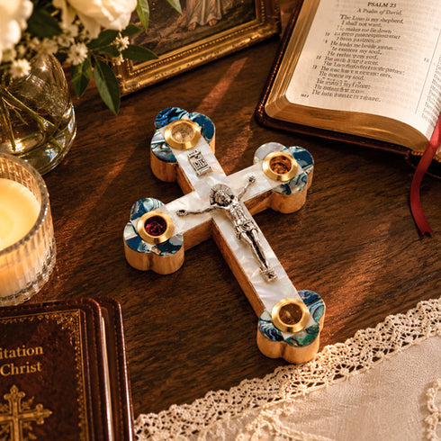 Decorative cross with religious text on a wooden surface with books and flowers.