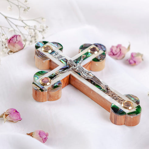 Olive wood cross with crucifix and Mother of pearl highlights on white backdrop.