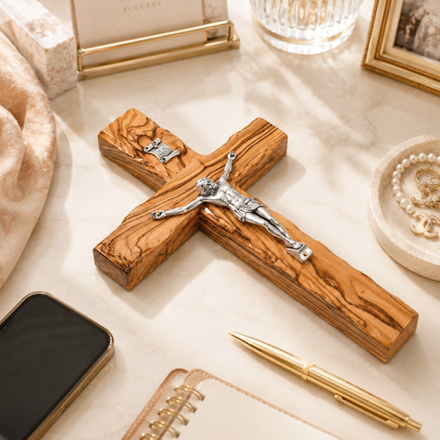 Wooden cross with Jesus figure on a table with phone, pen, and decorative items.
