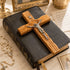 Wooden cross with Jesus figure on an closed bible, surrounded by religious items.