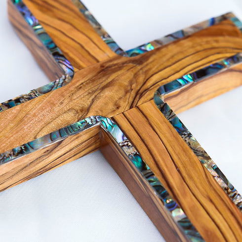 Close-up of a handmade olive wood Latin cross with shimmering nacre accents.
