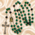 A rosary with green and black marbled beads, a silver-tone crucifix, and an oval medallion, on a beige fabric background.