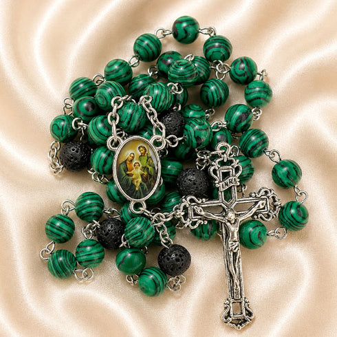 A green and black rosary with a silver-tone crucifix and a central medallion, on a satin fabric background.