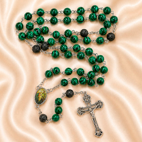 A green and black beaded rosary with a silver-tone crucifix and an oval medallion, on a satin fabric background.