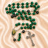 A green and black beaded rosary with a silver-tone crucifix and an oval medallion, on a satin fabric background.