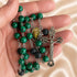 A close-up of a rosary in a hand, with green marbled and black lava stone beads, an oval medallion, and a silver-tone crucifix.