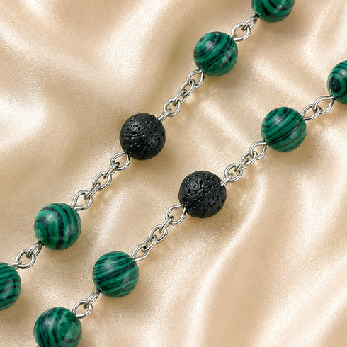 A beaded necklace with green malachite beads with black lava stone beads, on a beige satin fabric background.
