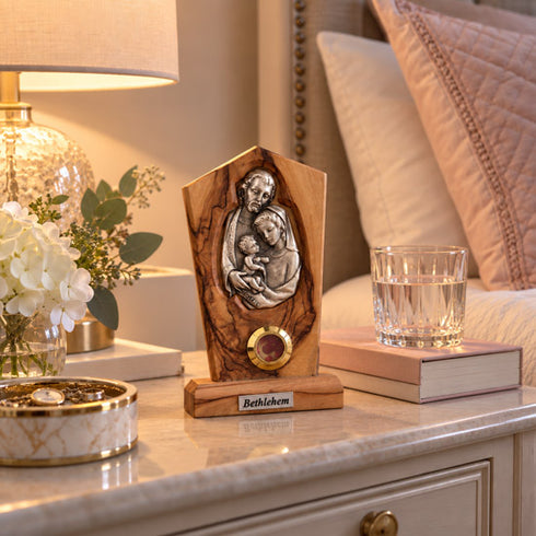 Holy Family olive wood plaque displayed in a bedroom, with warm decor softly blurred behind it